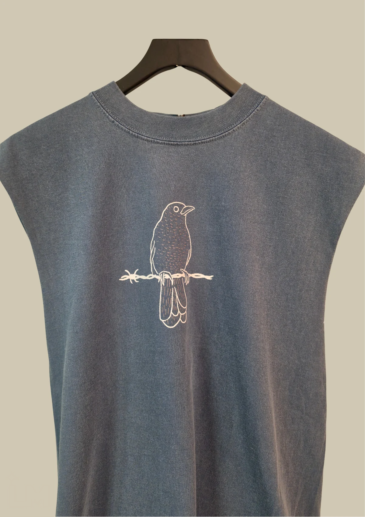 Camiseta sin mangas colgada, vista de cerca, con el mirlo de Isaac Orellana sobre un alambre de púas