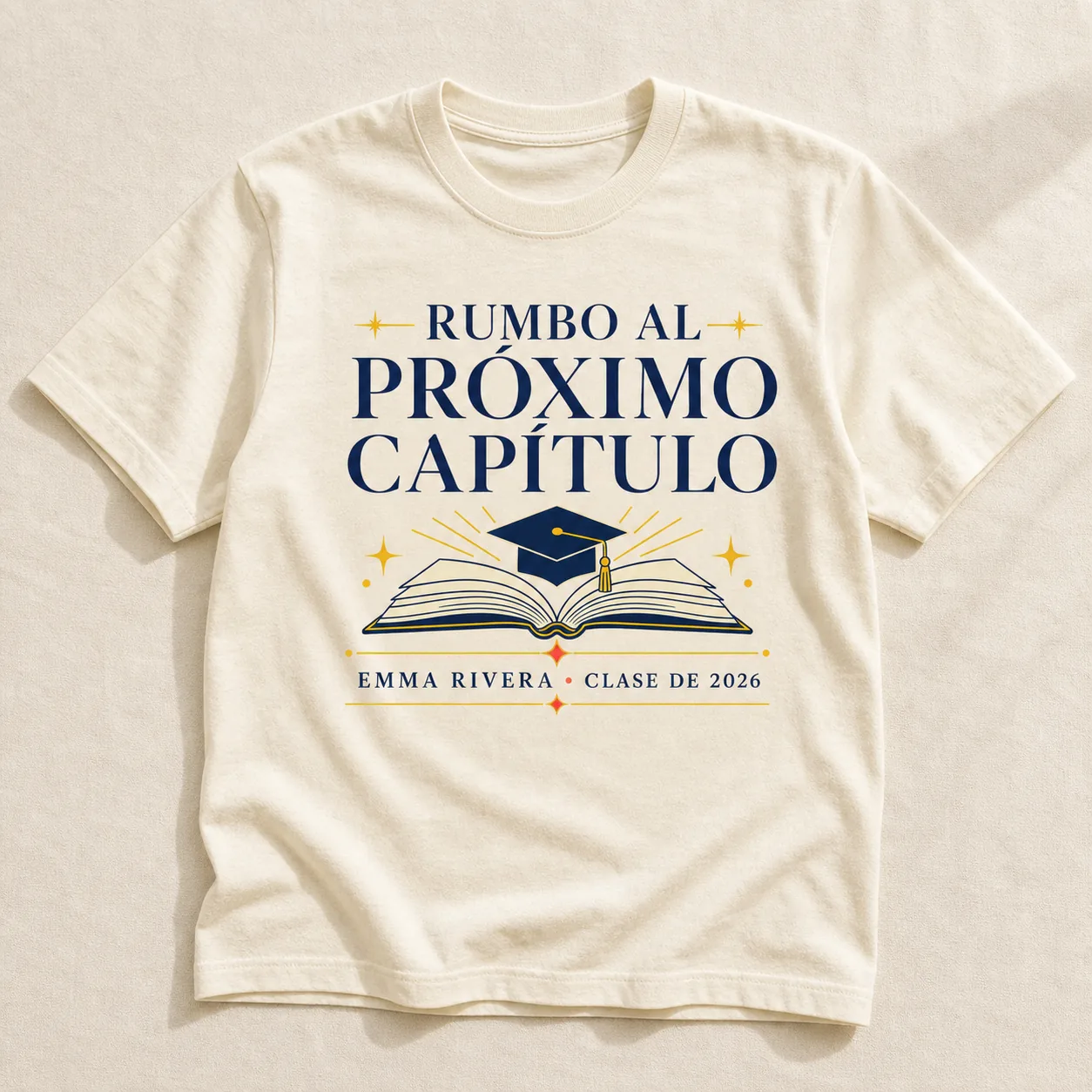 Camiseta Cream con el estampado «Rumbo al Próximo Capítulo»: un birrete sobre un libro abierto, con un nombre y un año de ejemplo debajo.