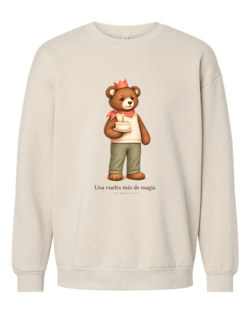 Cream sweatshirt with the «Una vuelta más de magia» print: a bear in a red paper crown and knit sweater holding a cake with a lit candle.