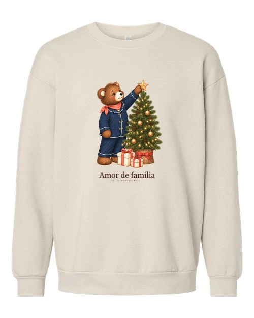 Sudadera Cream con el estampado «Amor de familia»: un oso en pijama azul coloca una estrella dorada en la punta de un árbol de Navidad con regalos debajo.